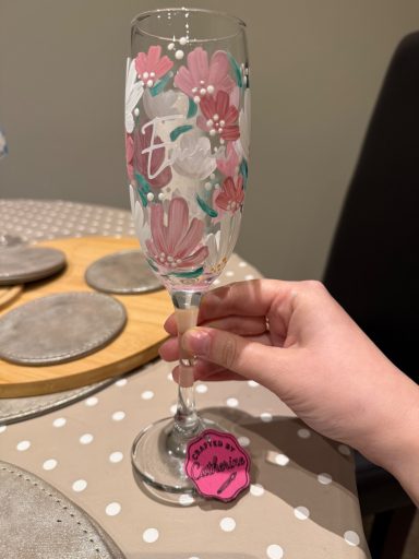A hand holding a decorated champagne flute with pink and green floral patterns.