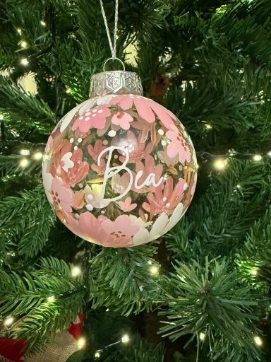 Pink floral ornament with the name "Bea" on a Christmas tree.