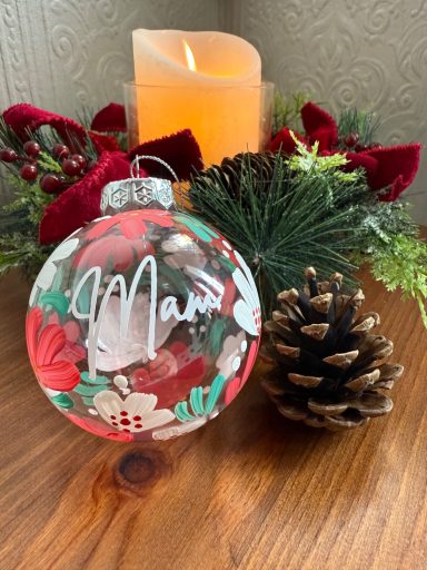 Clear Christmas bauble with floral design, placed beside a candle and pine cone.