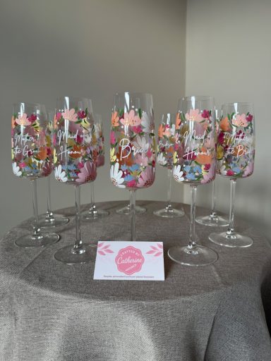 Six colourful champagne flutes with decorative floral patterns on a grey table.