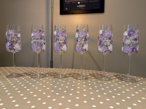 Five clear glasses with purple and white floral patterns arranged in a row on a polka-dot tablecloth.