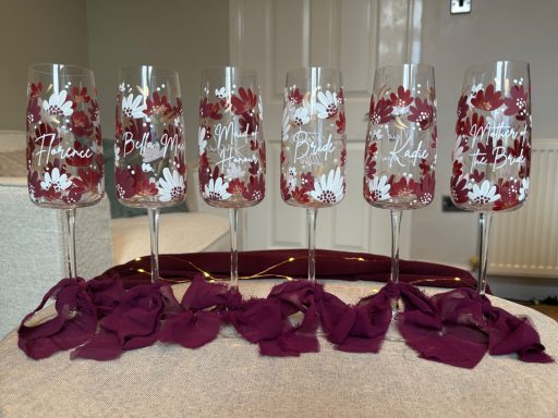 Six decorated champagne flutes with red floral patterns and burgundy ribbon accents.