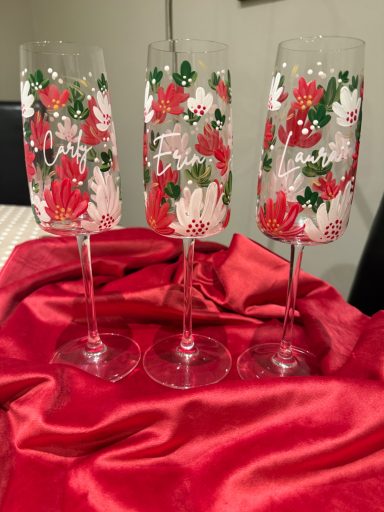 Three decorative champagne flutes with floral red and white designs on a red cloth.