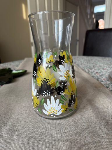 Glass vase decorated with yellow and white flowers on a table.