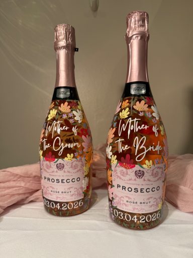 Two bottles of Prosecco with floral designs and pink foil caps on a soft pink background.