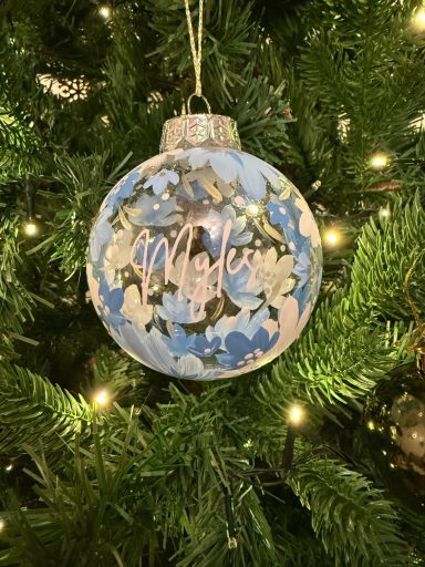 A blue and gold Christmas ornament with "Merry" nestled in a tree.
