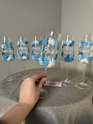 A hand holding a decorated champagne flute among four similar glasses.