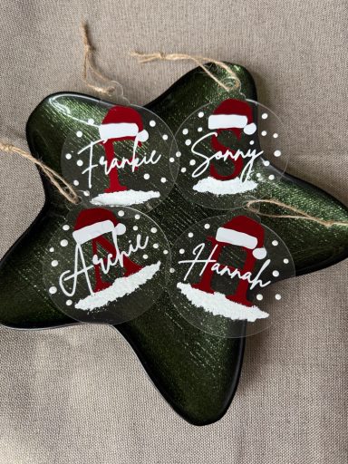 Four round ornaments with Santa hats and names: Frankie, Savy, Arhi, and Hank, on a star-shaped plate.