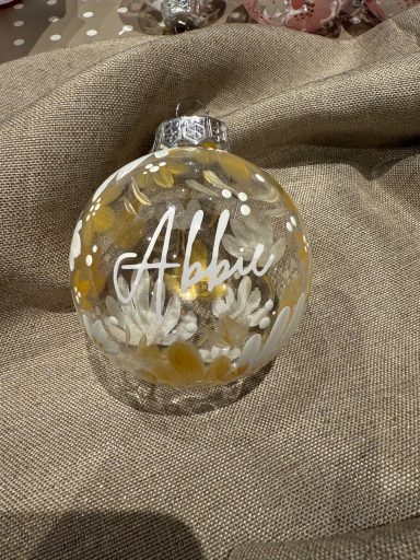 A clear glass ornament with the name "Abbie" and floral decorations.
